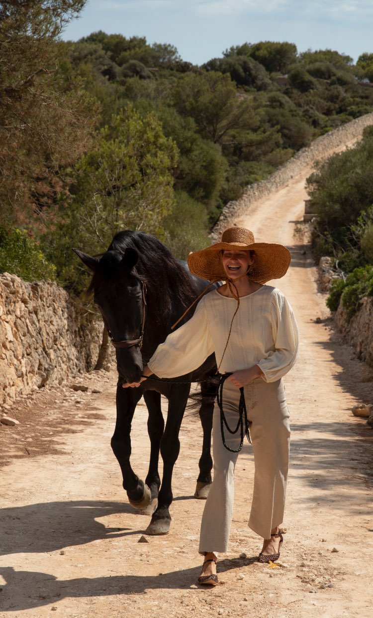 Lächelnde Frau, die ein Pferd über eine Straße auf Menorca führt. 