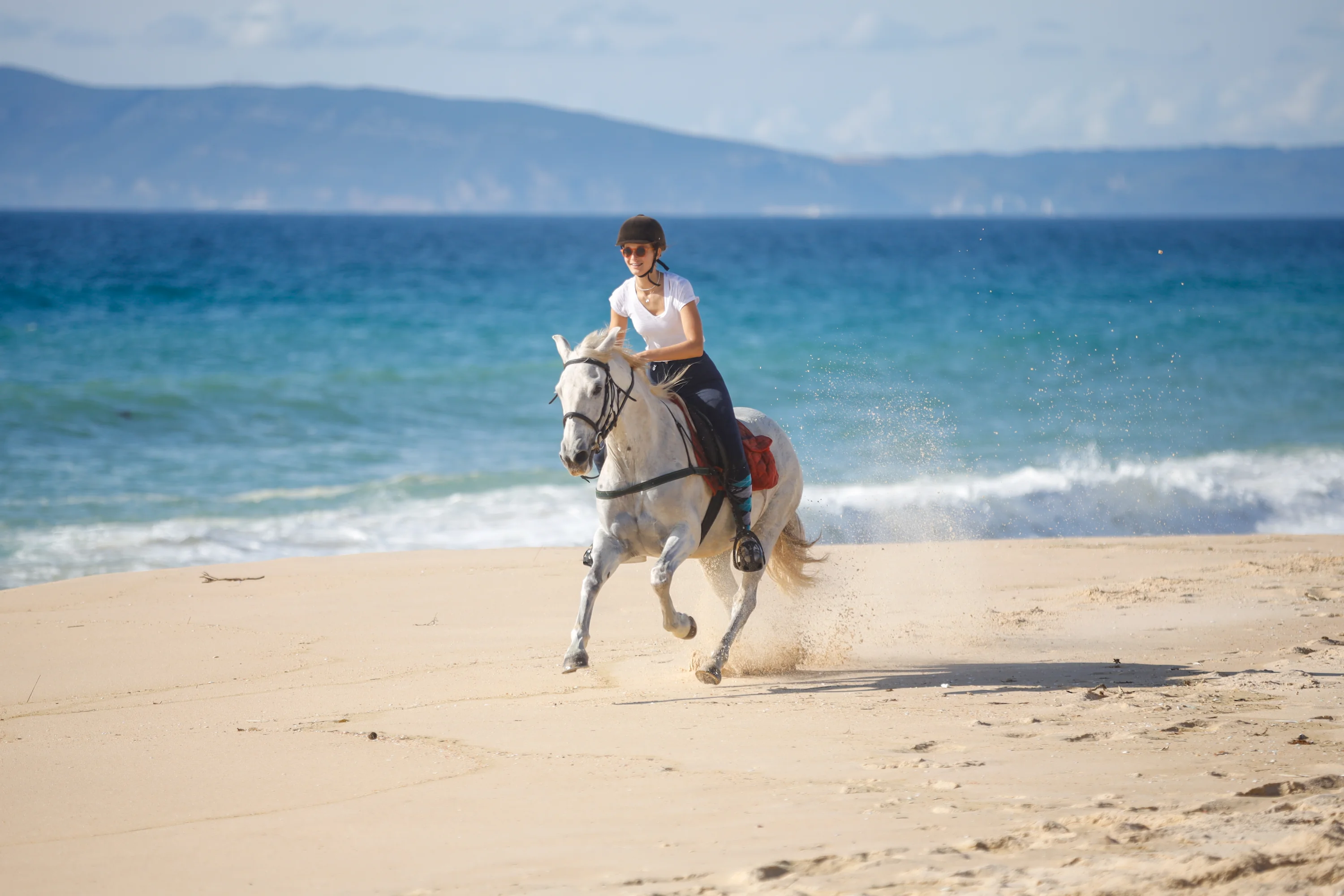 Woman riding a white horse on the beach in Comporta Portugal